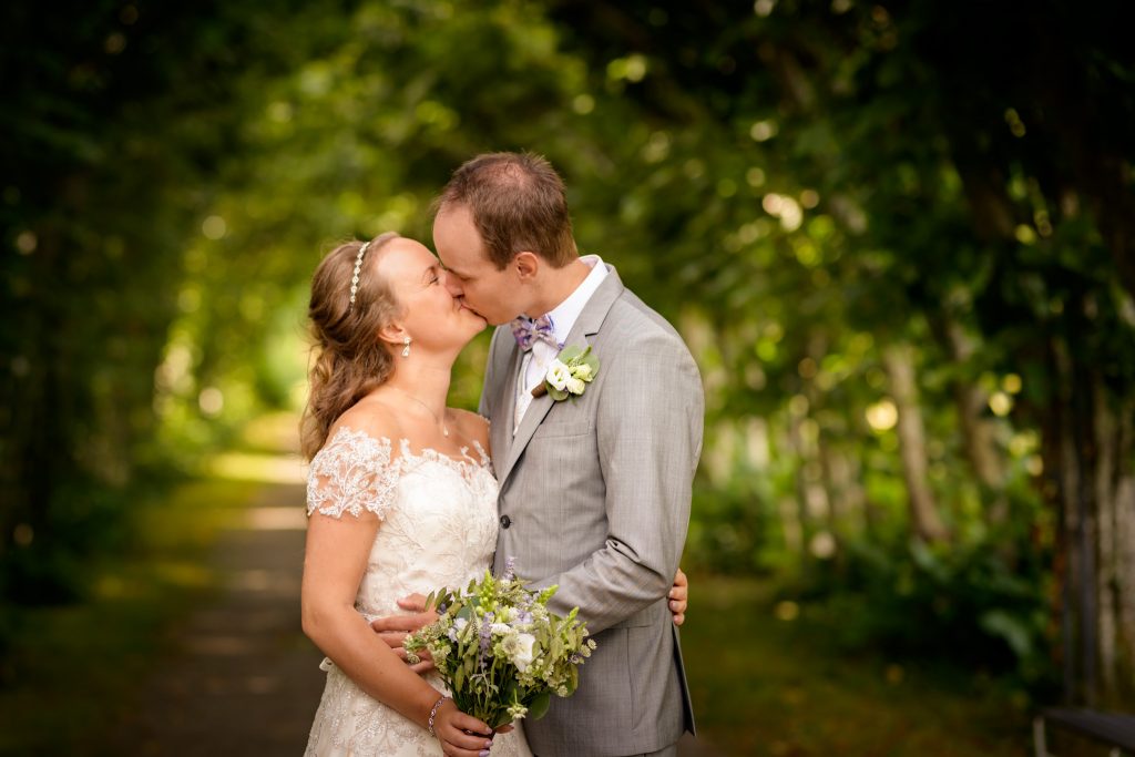 Brudpar kysser varandra på bröllopsporträtt under sin bröllopsfotografering med bröllopsfotograf sofia regnander i ett valv av träd och buskar i Ängsö