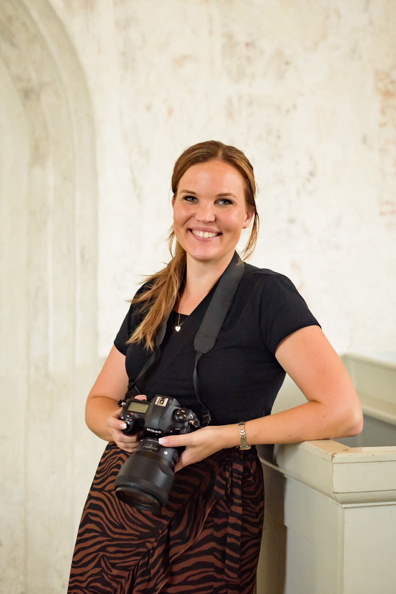 Bröllopsfotograf Sofia Regnander tittar in i kameran i väntan på fotografering av vigsel i kyrka. i handen håller hon sin kamera Nikon d850 med Sigma ART 85 mm 1.4 objektiv