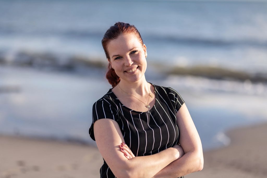 Fotograf Sofia Regnander vid havet på strand tittar in i kameran. Bilden togs vid Ystad Saltsjöbad