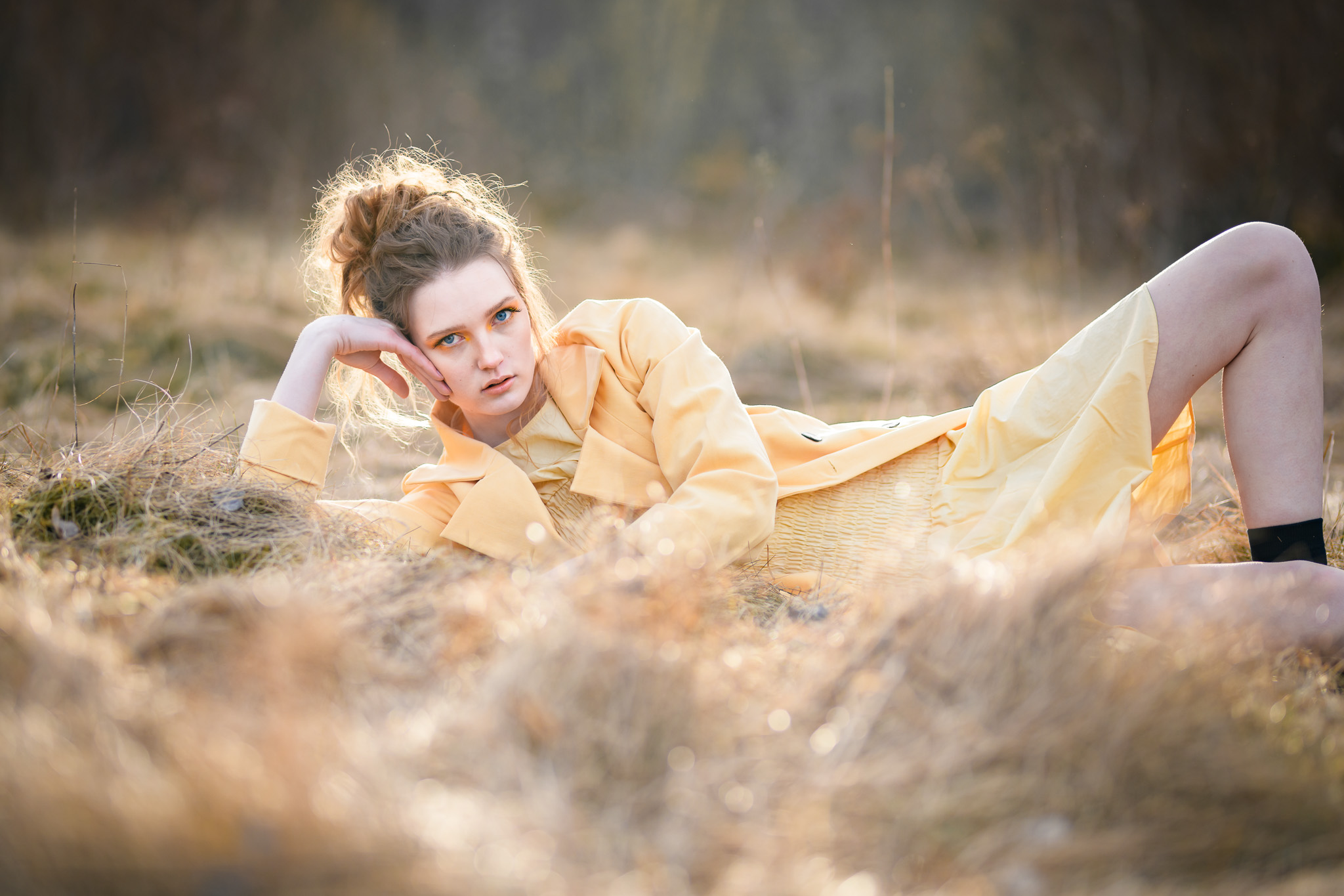 Egoboost-porträtt, Modefotografering. Modell ligger i gul rock på en äng med dött gräs i en kaxig pose.