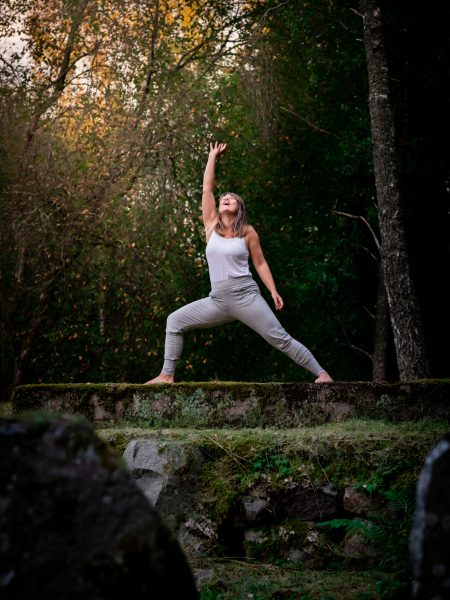 Kvinna i Yoga-position sträcker ena handen mot himlen och står barfota på gamma mossig ruin