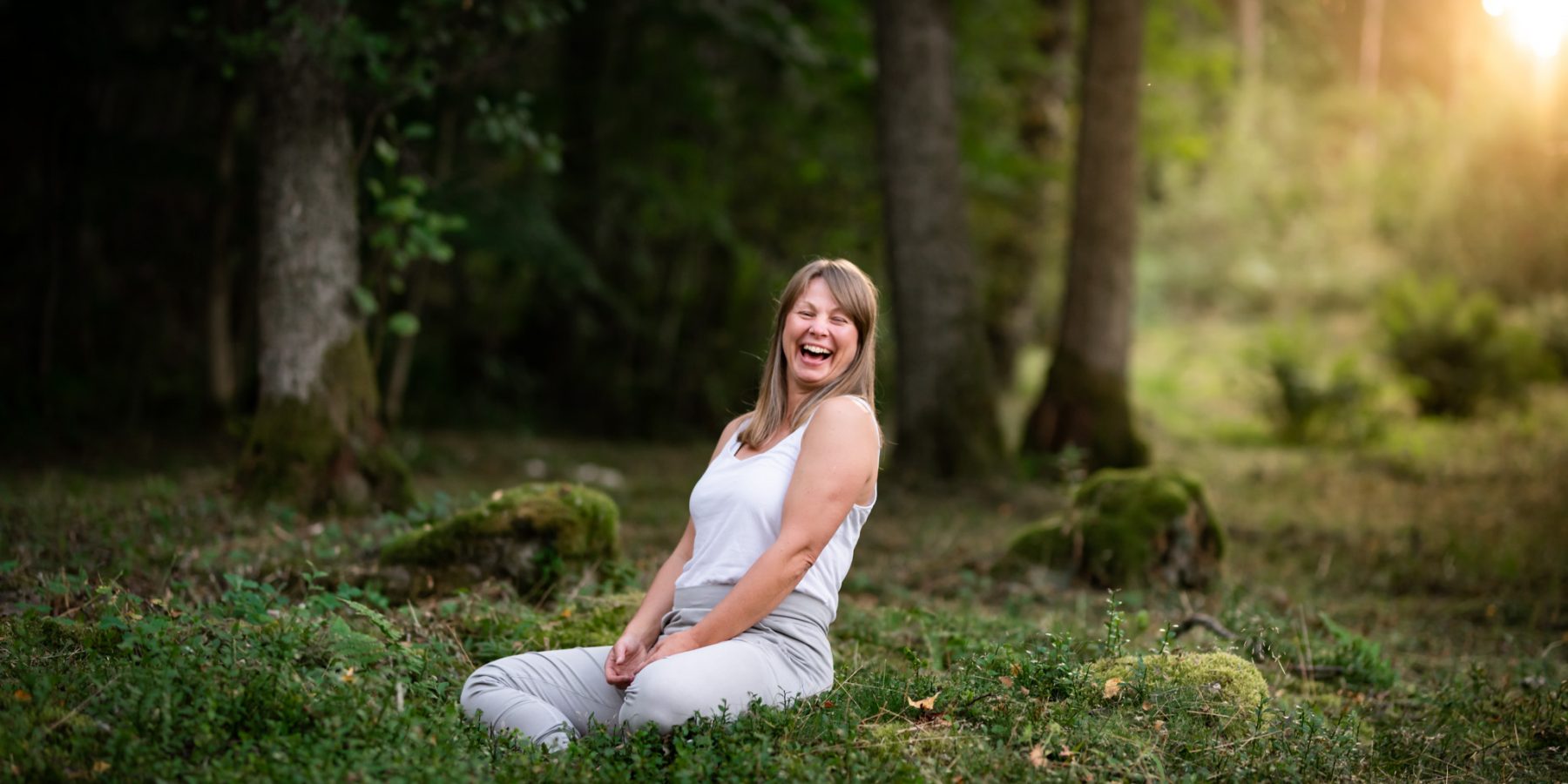 Yoga i skogen med kvällssol som mot ljus. Kvinna skrattar sig ur sin meditation. Egoboostfotografering för att stärka självkänsla