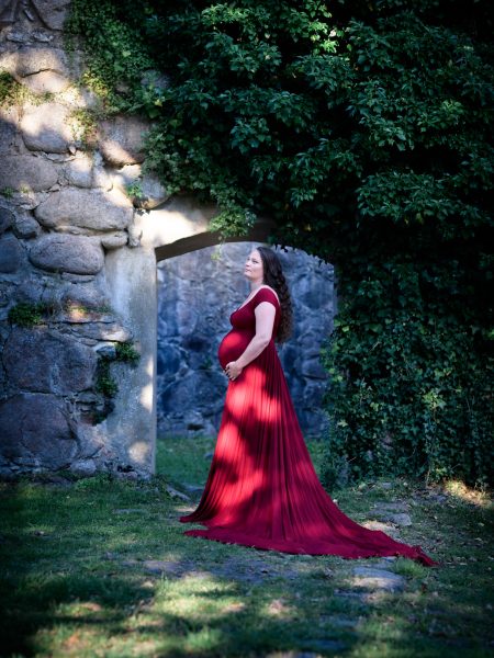 Gravid kvinna i röd klänning blickar upp mot ljuset i en ruin